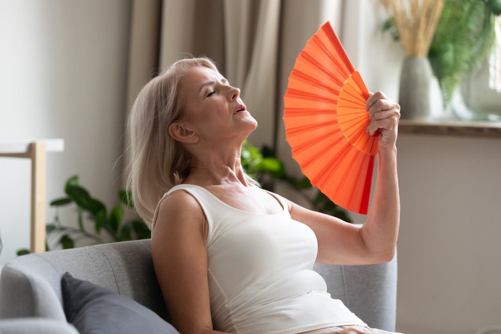 An older woman fans herself during a hot flash as she tries understanding perimenopause