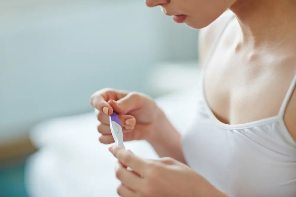 A woman looks down at a pregnancy test because understanding pregnancy test results can be hard