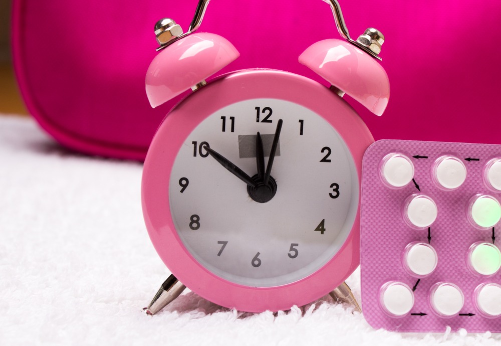 An image of a pink clock with a pack of birth control pills suggesting the idea of stopping birth control when trying to get pregnant